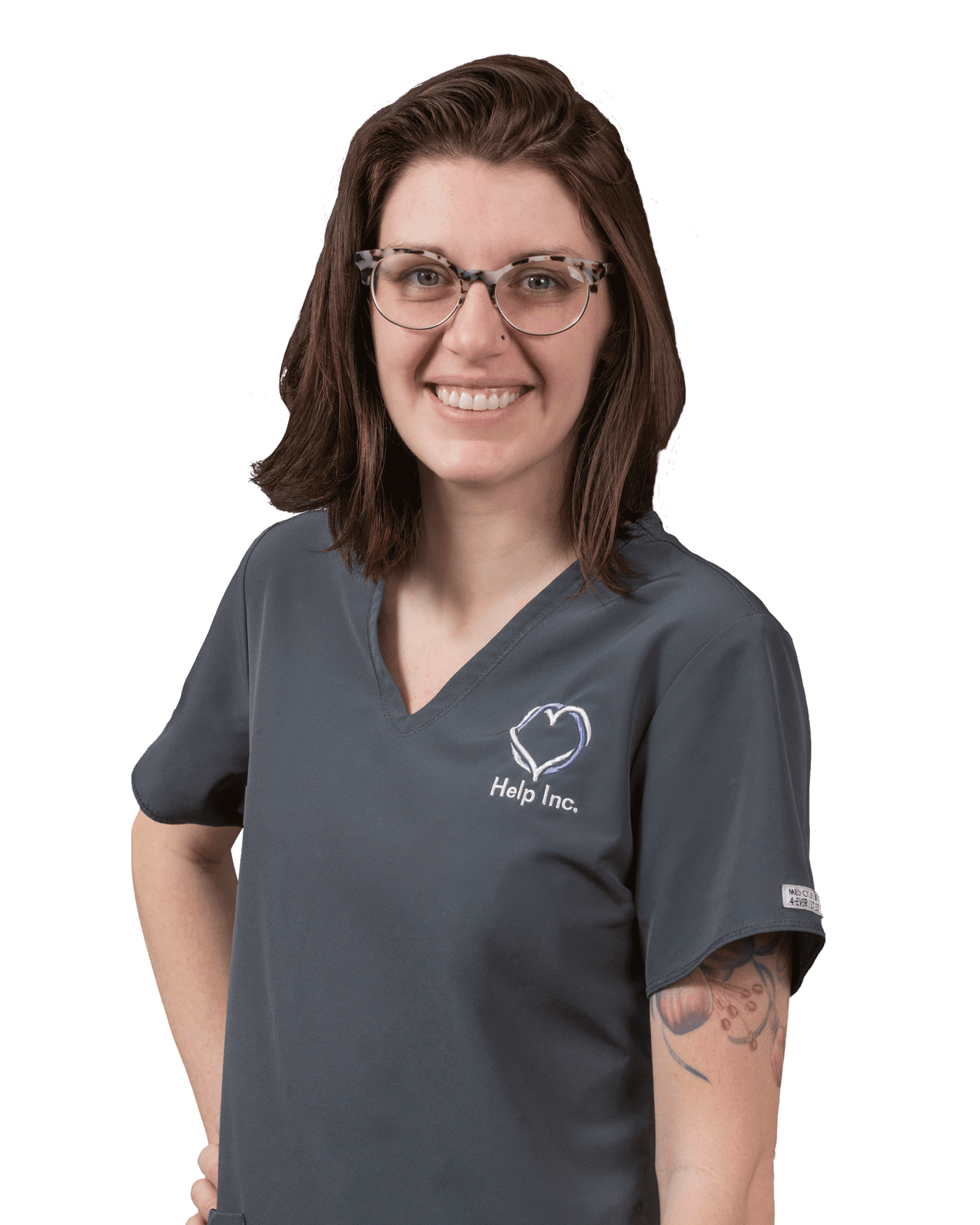 A woman wearing glasses and a gray scrub top with a "Help Inc." logo, standing and smiling at the camera.