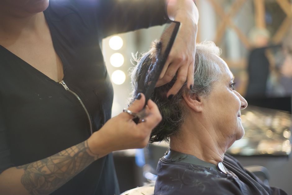 A hairstylist cuts and combs the hair of an older adult seated in a salon chair, with salon tools and mirrors in the background, highlighting the difference that personal care services can make in enhancing both comfort and appearance.