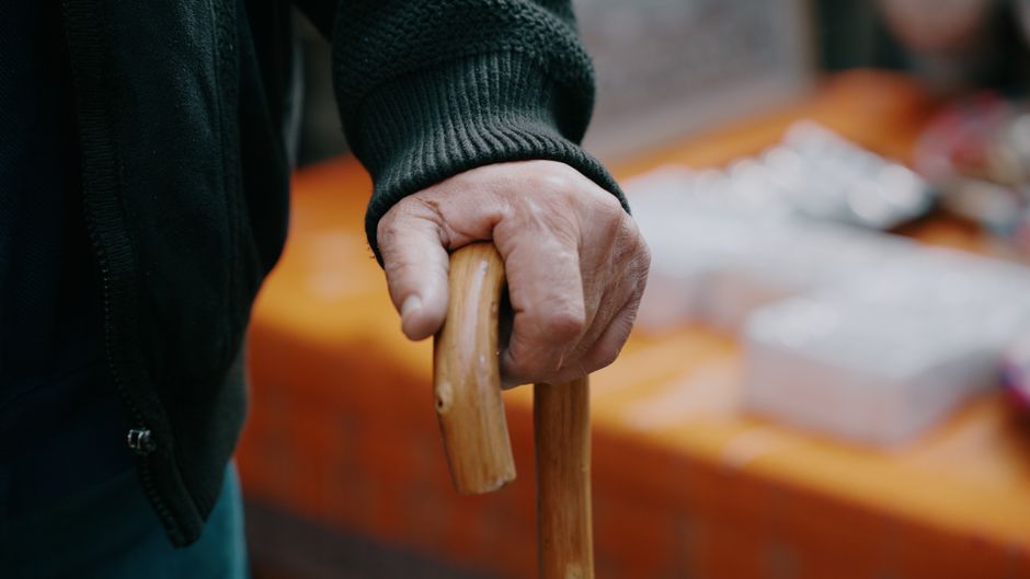 Close-up of a person’s hand resting on the handle of a wooden cane, providing mobility assistance.